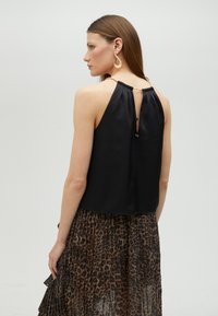 Black halter top with a pleated back, featuring a button closure and gold hardware. Paired with a sheer leopard print skirt.