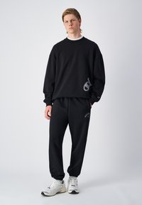 Zwarte katoenen sweatshirt met een boxy fit, met een logodetail. Gecombineerd met bijpassende zwarte joggingsbroek en witte sport sneakers.