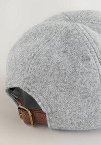 Grå følt hat med en rund form. Har en brun læderrem med en messingbuckle til justering. Synlige syninger langs sømmene.