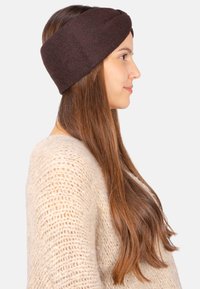 Bandeau en tricot marron avec un design torsadé, surface texturée et forme large, porté avec un pull de couleur claire.