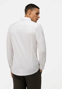 Witte longsleeve shirt met een puntige kraag, een gladde textuur en knopenmanchetten. De achterkant heeft een yoke en een schone, eenvoudige uitstraling.