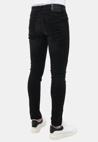 Zwarte skinny jeans met een gladde textuur, voorzien van een vijf-pocket ontwerp en een leren patch op de achterkant van de taille. Gedragen met witte sneakers.