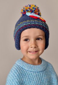 Bonnet en tricot bleu marine avec un pompon coloré, des patchs décoratifs et des rayures horizontales vives. Pull bleu texturé avec un col large.
