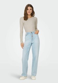 Jeans alta vita blu chiaro con una vestibilità dritta, dotati di chiusura frontale a cinque bottoni e delicate sfumature. Abbinati a un top fitted beige.