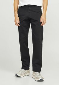 Schwarze Hosen aus gewebtem Stoff mit glatter Textur, geradem Schnitt, seitlichen Taschen und Reißverschluss, kombiniert mit silbernen Sportschuhen.