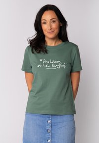 Groen T-shirt met korte mouwen, gemaakt van zacht materiaal, met witte bedrukte tekst 'Das Leben ist kein Ponyhof.' voor een casual look.