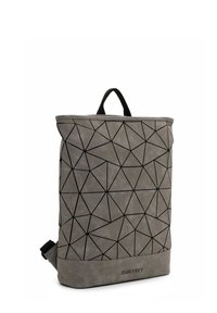 Mochila gris con líneas geométricas negras, asa superior y logo "SURI FREY" en el panel frontal inferior.