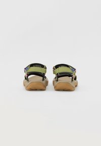 Green sandals with black straps and purple accents. The sole is tan with a textured grip pattern and adjustable straps for a secure fit.