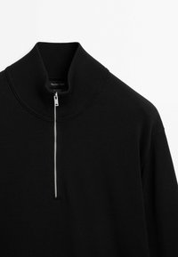Black cotton pullover with a high collar and a silver zipper at the front. Textured, ribbed neckline. Simple, clean design.