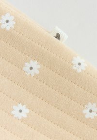 Tissu beige avec des lignes horizontales cousues et de petites fleurs de marguerite blanches dispersées sur toute la surface.