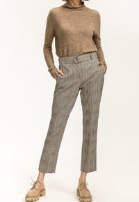 Beiger Strickpullover und graue karierte Hose mit einem eng anliegenden Gürtel. Die Schuhe sind hellbraun mit einer klobigen Sohle. Standardpassform, schlankes Design.