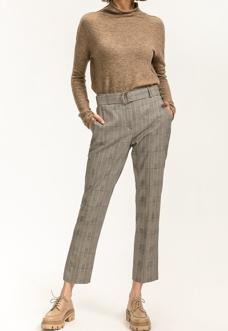 Beiger Strickpullover und graue karierte Hose mit einem eng anliegenden Gürtel. Die Schuhe sind hellbraun mit einer klobigen Sohle. Standardpassform, schlankes Design.