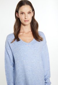 Pulover bleu deschis, cu decolteu în V, cu o croială lejeră. Textură moale, manșoni lungi cu umeri căzuți, design minimalist, fără modele sau accente.