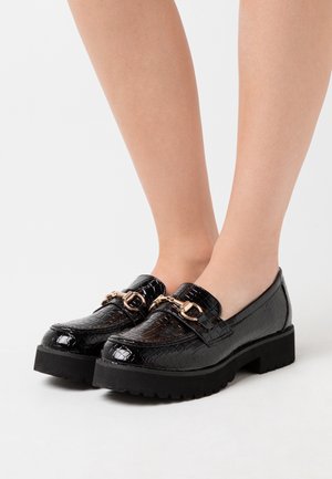 Des mocassins en cuir synthétique noir laqué présentent un motif crocodile texturé, des accessoires en ton doré et une semelle extérieure noire épaisse.