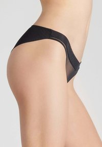 Culotte de bikini noire en matériau lisse et extensible. Présente une coupe taille basse et une couverture arrière minimale, soulignant le confort et l'ajustement.