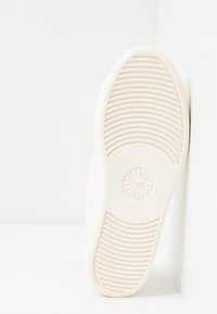 Biała podeszwa sneakersów z poziomymi rowkami, okrągłym logo i teksturowanymi wzorami zapewniającymi przyczepność. Czysty, minimalistyczny design z gładkim wykończeniem.