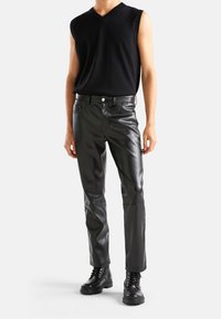 Svart ärmlös stickad topp i kombination med svarta läderbyxor med rak passform och svarta snörstövlar, med en mjuk textur och enkel design.