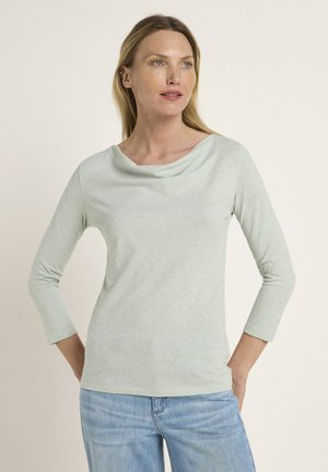 Hellgrünes Langarmoberteil mit einem Cowl-Neck-Design. Weiche Textur, taillierte Silhouette und ein dezentes Melange-Muster. Kombiniert mit Jeans.
