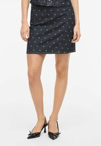 Jupe mini en denim avec une base bleu foncé, ornée de pois bleu clair. Le design est épuré, avec une coupe droite et sans ornements supplémentaires.