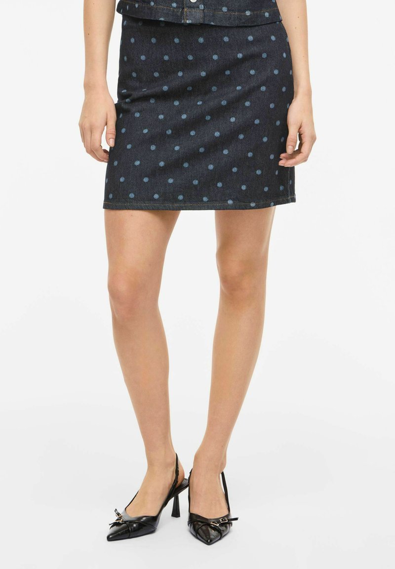 Jupe mini en denim avec une base bleu foncé, ornée de pois bleu clair. Le design est épuré, avec une coupe droite et sans ornements supplémentaires.