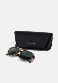 Ochelari de soare Michael Kors cu un cadru octagonal în model de țestoasă verde închis, însoțiți de un toc din piele neagră cu un logo.