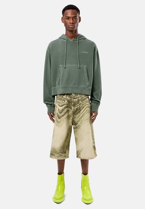 Haut à capuche vert coupé avec cordons, associé à un short métallique doré et des bottines vert vif. Textures lisses avec des couleurs distinctes.