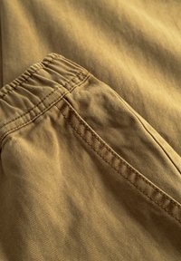 Beiges Hahnentritt-Musterstoff mit elastischem Bund und Seitentasche, sichtbare Nähte. Nahaufnahme.