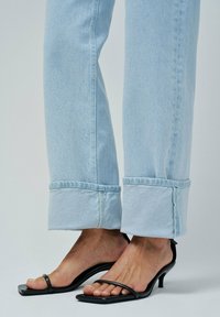 Jeans de mezclilla azul claro con dobladillo doblado y borde sin rematar, combinados con sandalias de tacón abiertas negras con tiras delgadas.