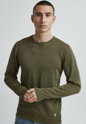 Pull-over en vert olive avec des manches longues, un col et des poignets côtelés, un corps texturé et un patch logo en bas.