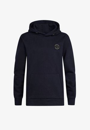 Marineblauer Hoodie mit einer Fronttasche und einem Logo-Patch, kombiniert mit hellblauen Jeans und weißen Sneakern. Der Stoff wirkt weich und strukturiert.