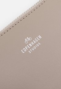 Bolsa de piel texturizada color beige claro, con cremallera plateada y logo impreso en blanco "COPENHAGEN STUDIOS" sobre un gráfico de bicicleta.