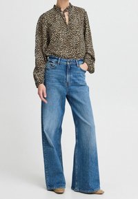 Blusa leopardata con dettaglio a chiave, abbinata a jeans blu a gamba larga con vita alta. Denim chiaro con una superficie liscia.