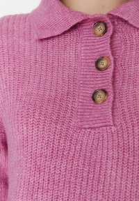 Gestrickter rosa Pullover mit einem Kragen und drei Holzknöpfen. Die Textur ist weich und leicht gerippt.