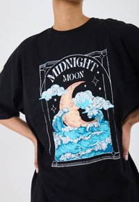 Černé oversized tričko s grafickou potiskem vln a srpku měsíce s textem "MIDNIGHT MOON" v vrstveném designu.