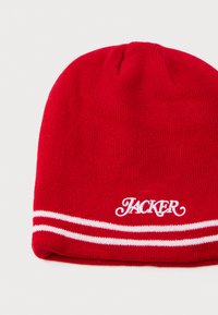 Gorro de punto rojo con una textura suave, con rayas blancas en el puño y "JACKER" bordado en un estilo de letra cursiva.