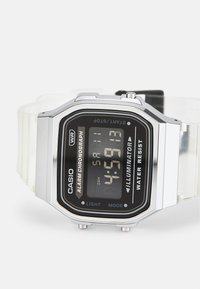 Montre numérique Casio avec un cadran noir, boîtier en métal argenté, bracelet en résine transparent, affichage éclairé et fonctionnalités telles que l'alarme et la résistance à l'eau.