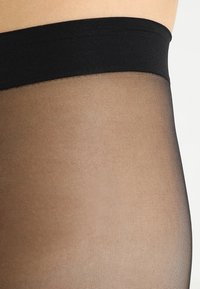 Prozirne crne tajice s mekanom, glatkom teksturom, koje imaju širok pojas za udobnost. Materijal je lagan i blago proziran.