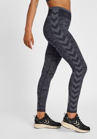 Höga tights i mörkgrått med ett mönster av zick-zack och djurtryck. Tillverkade av elastisk tyg, tillsammans med svarta sportskor.