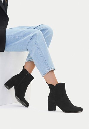 Mustad seemiskitahvel saabastega blokiašnaga ja luku sulgemine. Omadusteks on lainelise äärega krae ja sile pind, kombineeritud heledate teksadega.