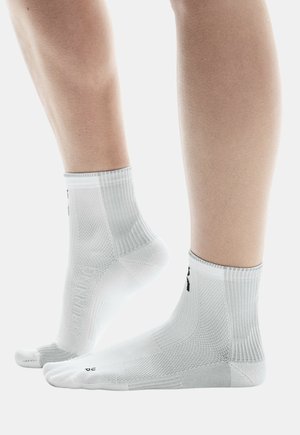 Chaussettes de sport blanches avec un bord côtelé, un matériau texturé et un logo en accent. Longueur cheville avec une coupe ajustée pour le confort.