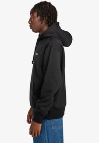 Black hoodie featuring a kangaroo pocket, drawstring hood, and a logo on the chest. Fabric appears soft and textured.