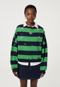 Groen en marine gestreepte sweater met versieringen, met een ronde halslijn, oversized pasvorm en ribgebreide mouwen, gedragen over een witte overhemd met kraag.