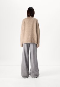 Beige oversized knit sweater with a high collar, paired with loose gray trousers that drape at the ankles, creating a relaxed silhouette.