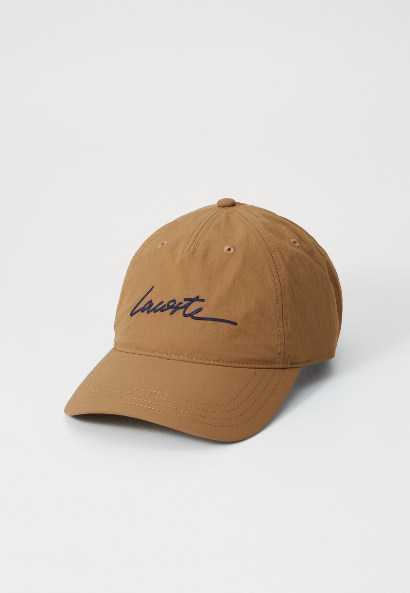 Casquette en coton marron avec visière incurvée, arborant un logo brodé bleu sur l'avant et des trous de ventilation sur les côtés.