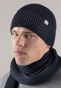 Navy knitted beanie with vertical ribbing, paired with a matching thick scarf. Both made of textured fabric, providing warmth and coverage.