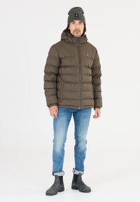 Brun puffjacka med hög krage, dragkedjestängning och ribbade muddar. Matchad med ljusblå jeans och svarta Chelsea boots. Grå mössa med logotyp.