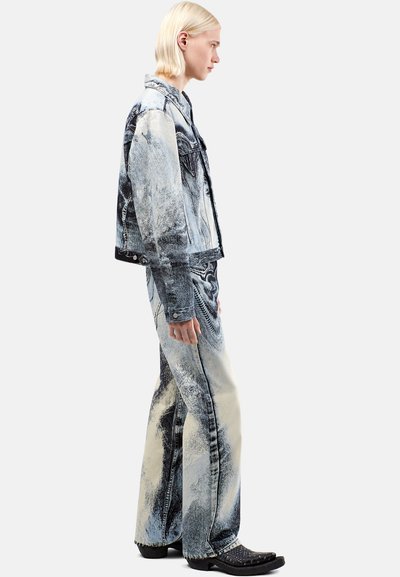 Chaqueta de mezclilla y jeans acampanados en azul y crema con un patrón abstracto. La chaqueta tiene un corte clásico; los jeans presentan costuras en contraste y piernas anchas.