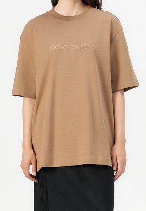 Bruin katoenen T-shirt met korte mouwen, ronde hals en een tonale "adidas"-logo aan de voorkant. Relaxte pasvorm, gladde textuur.