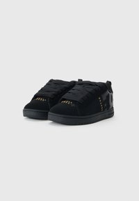 Zapatillas negras con un upper de ante y textil, puntera redonda, suela de goma gruesa y detalles de tachuelas doradas a los lados.