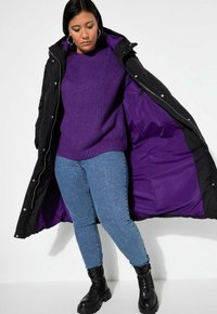 Svart vadderad jacka med lila foder, bärs över en lila stickad tröja och ljusblå jeans med pärlaccenter. Svarta grova snörstövlar.